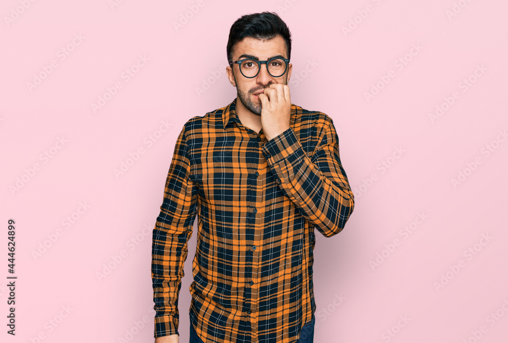 Hispanic man with beard wearing casual clothes and glasses looking stressed and nervous with hands on mouth biting nails. anxiety problem. Hispanic man with beard wearing casual clothes and glasses looking stressed and nervous with hands on mouth biting nails. anxiety problem.