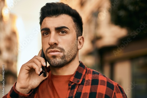 Young hispanic man with serious expression talking on the smartphone at the city.