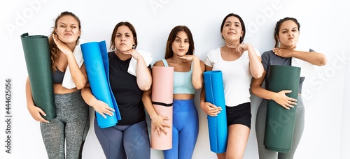 Group of women holding yoga mat standing over isolated background cutting throat with hand as knife, threaten aggression with furious violence