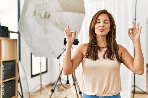 Young latin woman standing at photography studio relax and smiling with eyes closed doing meditation gesture with fingers. yoga concept.