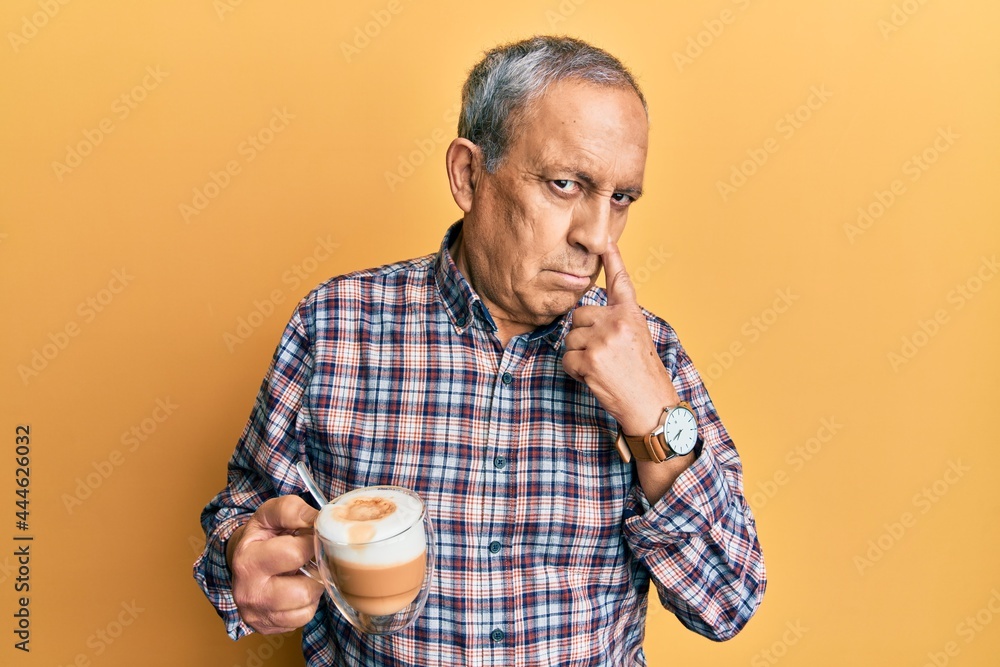 Handsome senior man with grey hair drinking a cup coffee pointing to the eye watching you gesture, suspicious expression Handsome senior man with grey hair drinking a cup coffee pointing to the eye watching you gesture, suspicious expression