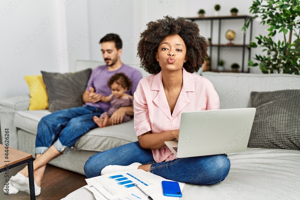 Mother of interracial family working using computer laptop at home looking at the camera blowing a kiss on air being lovely and sexy. love expression. Mother of interracial family working using computer laptop at home looking at the camera blowing a kiss on air being lovely and sexy. love expression.