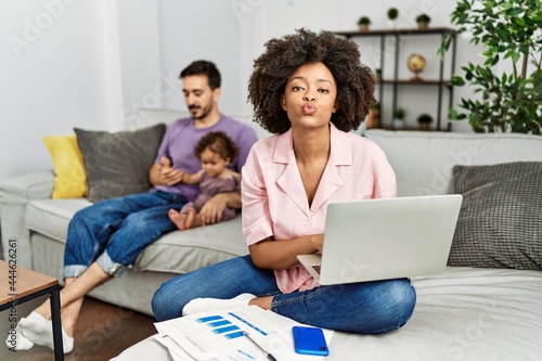 Mother of interracial family working using computer laptop at home looking at the camera blowing a kiss on air being lovely and sexy. love expression.