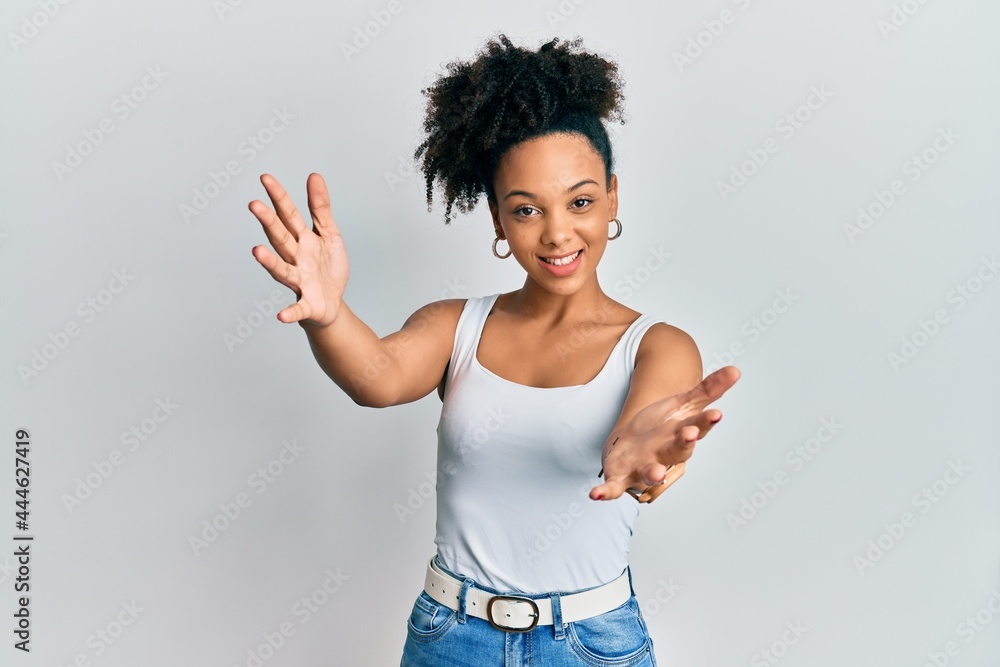 Young african american girl wearing casual style with sleeveless shirt looking at the camera smiling with open arms for hug. cheerful expression embracing happiness. Young african american girl wearing casual style with sleeveless shirt looking at the camera smiling with open arms for hug. cheerful expression embracing happiness.