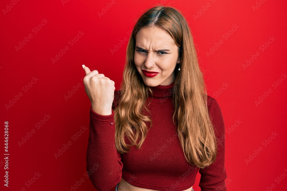 Young blonde woman wearing turtleneck sweater angry and mad raising fist frustrated and furious while shouting with anger. rage and aggressive concept. Young blonde woman wearing turtleneck sweater angry and mad raising fist frustrated and furious while shouting with anger. rage and aggressive concept.