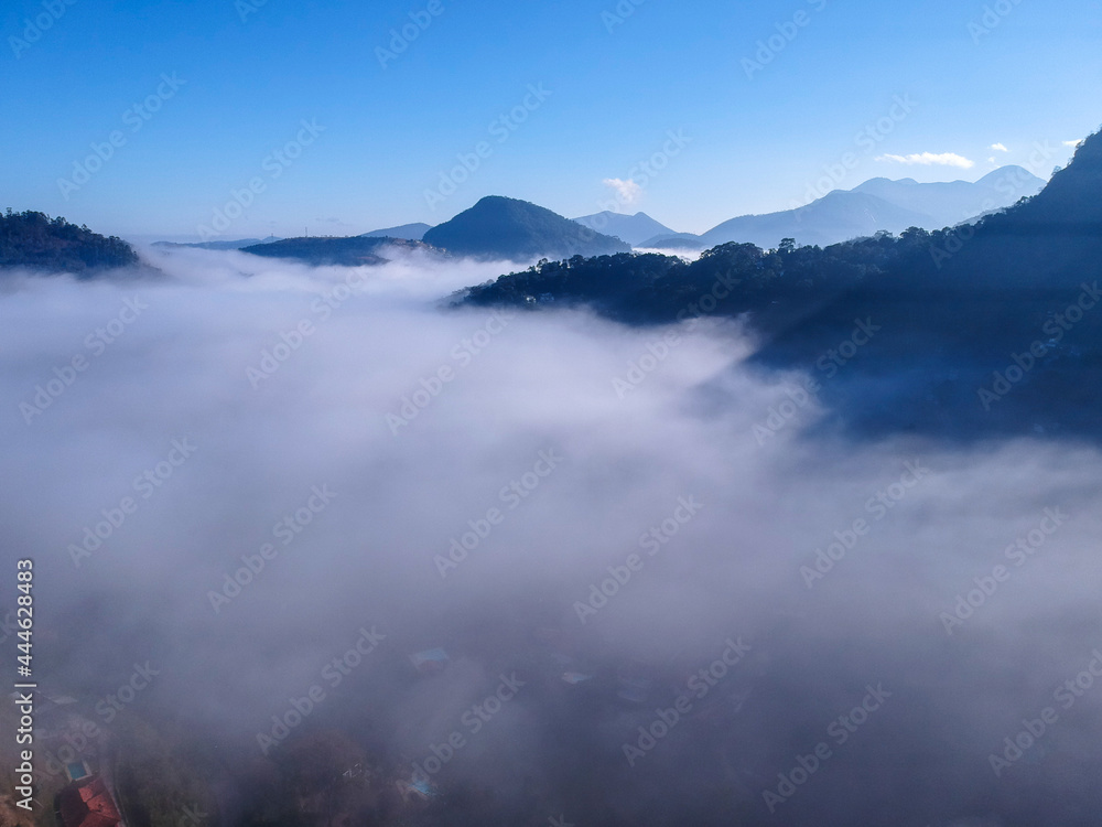 Aerial view of Itaipava, Petrópolis. Early morning with a lot of fog in the city. Mountains with blue sky and clouds around Petrópolis, mountainous region of Rio de Janeiro, Brazil. Drone photo. 