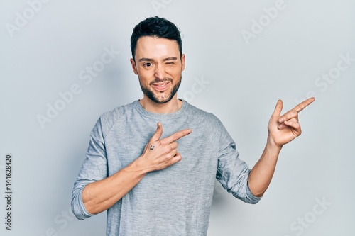 Young hispanic man pointing with fingers to the side winking looking at the camera with sexy expression, cheerful and happy face.