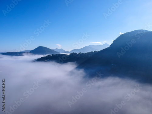 Aerial view of Itaipava, Petrópolis. Early morning with a lot of fog in the city. Mountains with blue sky and clouds around Petrópolis, mountainous region of Rio de Janeiro, Brazil. Drone photo.  © Diego