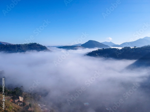 Aerial view of Itaipava, Petrópolis. Early morning with a lot of fog in the city. Mountains with blue sky and clouds around Petrópolis, mountainous region of Rio de Janeiro, Brazil. Drone photo.   © Diego
