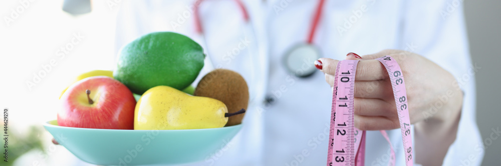 Nutritionist doctor holds plate of fruit and centimeter Nutritionist doctor holds plate of fruit and centimeter