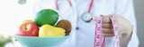 Nutritionist doctor holds plate of fruit and centimeter