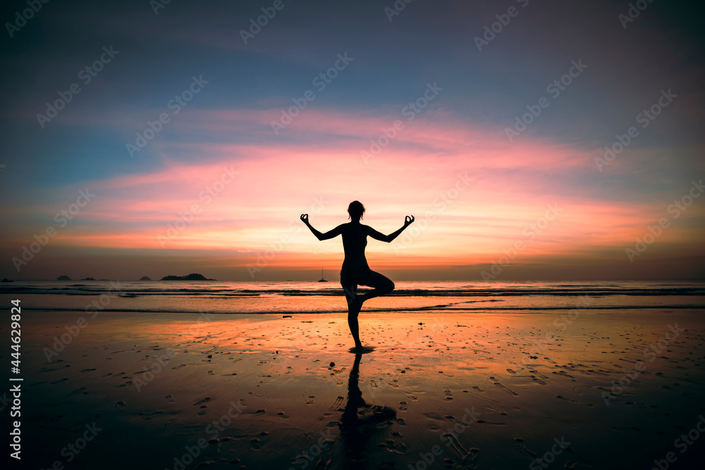 Silhouette of yoga woman on the ocean beach at surreal sunset.