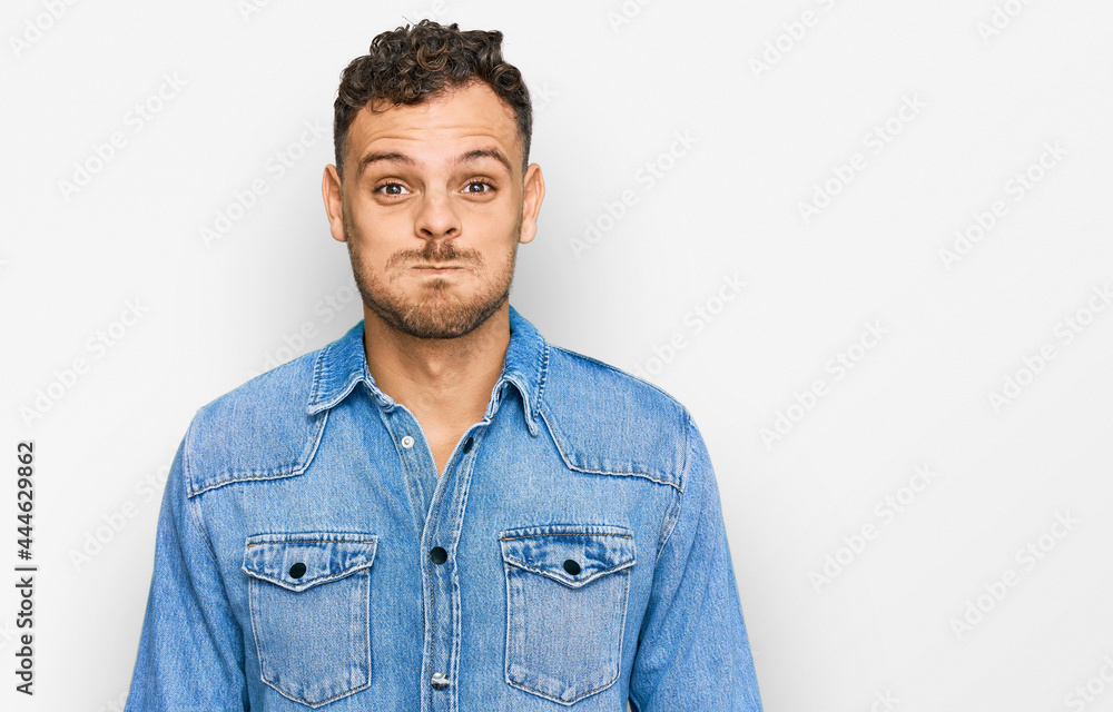 Young hispanic man wearing casual denim jacket puffing cheeks with funny face. mouth inflated with air, crazy expression. Young hispanic man wearing casual denim jacket puffing cheeks with funny face. mouth inflated with air, crazy expression.