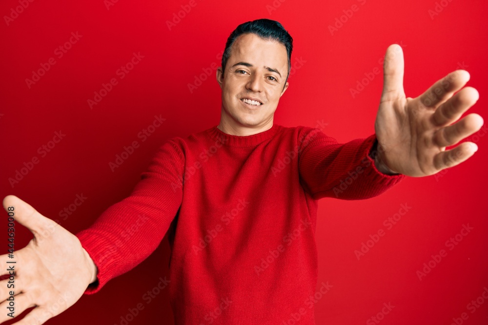 Handsome young man wearing casual winter sweater looking at the camera smiling with open arms for hug. cheerful expression embracing happiness. Handsome young man wearing casual winter sweater looking at the camera smiling with open arms for hug. cheerful expression embracing happiness.