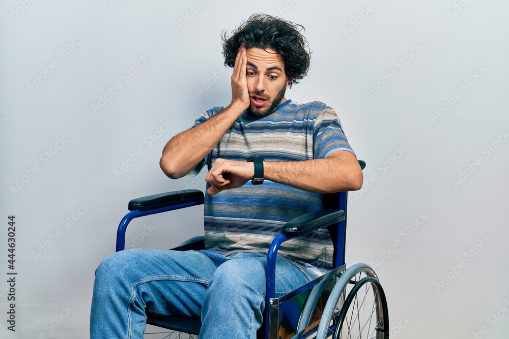 Handsome hispanic man sitting on wheelchair looking at the watch time worried, afraid of getting late Handsome hispanic man sitting on wheelchair looking at the watch time worried, afraid of getting late