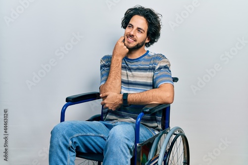 Handsome hispanic man sitting on wheelchair with hand on chin thinking about question, pensive expression. smiling and thoughtful face. doubt concept.