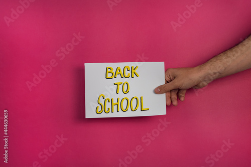 A closeup shot of a man holding a paper with the word "BACK TO SCHOOL" on a fuchsia background
