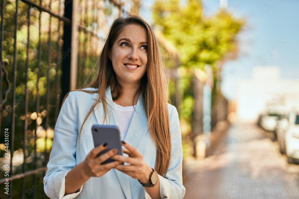 Young blonde businesswoman smiling happy using smartphone at the city. Young blonde businesswoman smiling happy using smartphone at the city.