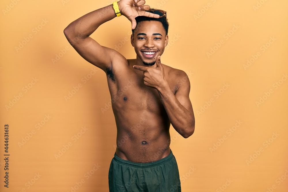 Young african american man wearing swimwear and swimmer glasses smiling making frame with hands and fingers with happy face. creativity and photography concept.