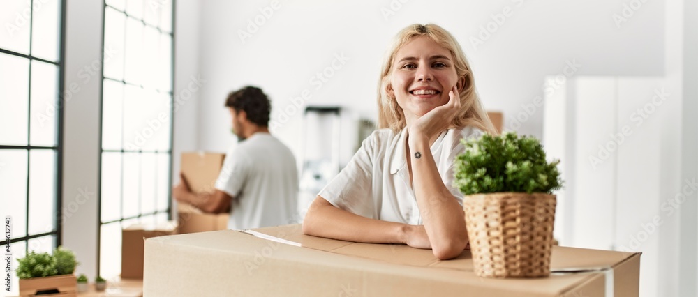 Young woman smiling happy leaning on cardboard at new home. Young woman smiling happy leaning on cardboard at new home.