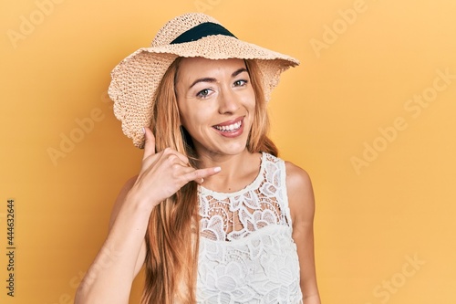 Young caucasian woman wearing summer hat smiling doing phone gesture with hand and fingers like talking on the telephone. communicating concepts.