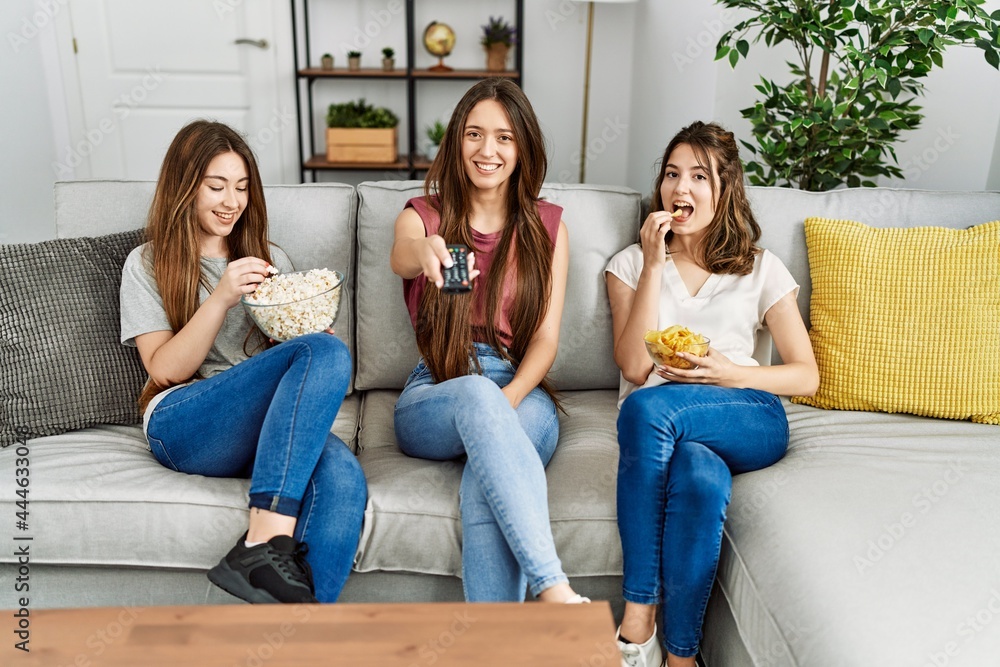 Three young hispanic woman smiling happy watching film eating popcorn and chips potatoes at home. Three young hispanic woman smiling happy watching film eating popcorn and chips potatoes at home.