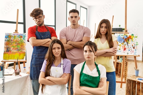 Group of five hispanic artists at art studio skeptic and nervous, disapproving expression on face with crossed arms. negative person.
