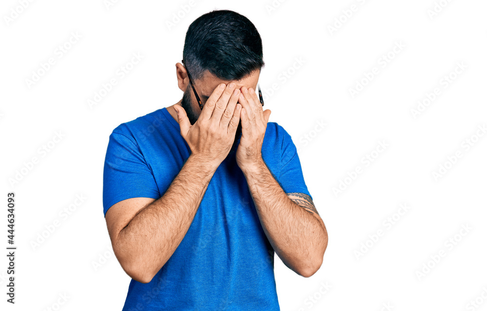 Hispanic man with beard wearing casual t shirt and glasses with sad expression covering face with hands while crying. depression concept. Hispanic man with beard wearing casual t shirt and glasses with sad expression covering face with hands while crying. depression concept.