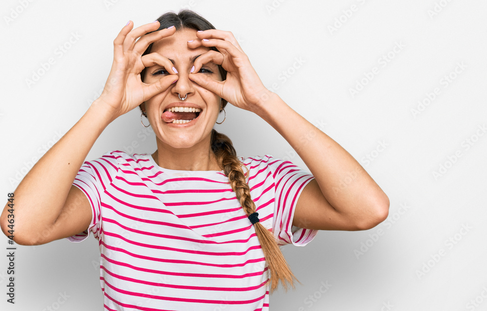 Young hispanic woman wearing casual clothes doing ok gesture like binoculars sticking tongue out, eyes looking through fingers. crazy expression. Young hispanic woman wearing casual clothes doing ok gesture like binoculars sticking tongue out, eyes looking through fingers. crazy expression.
