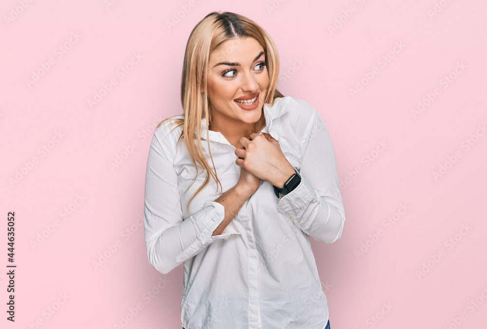 Young caucasian woman wearing casual clothes laughing nervous and excited with hands on chin looking to the side Young caucasian woman wearing casual clothes laughing nervous and excited with hands on chin looking to the side