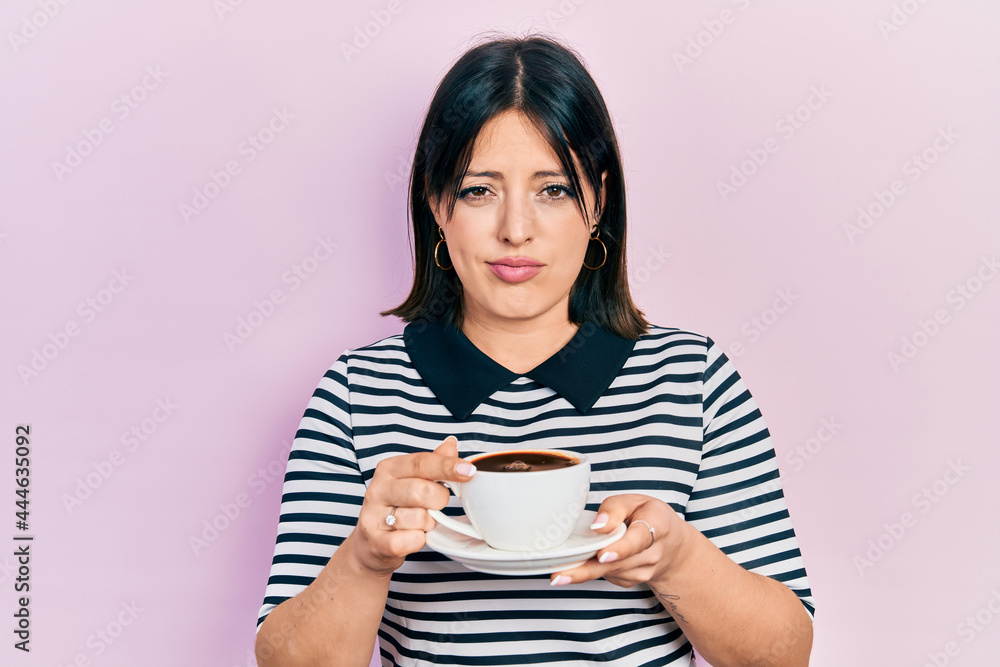 Young hispanic woman drinking a cup of coffee skeptic and nervous, frowning upset because of problem. negative person. Young hispanic woman drinking a cup of coffee skeptic and nervous, frowning upset because of problem. negative person.