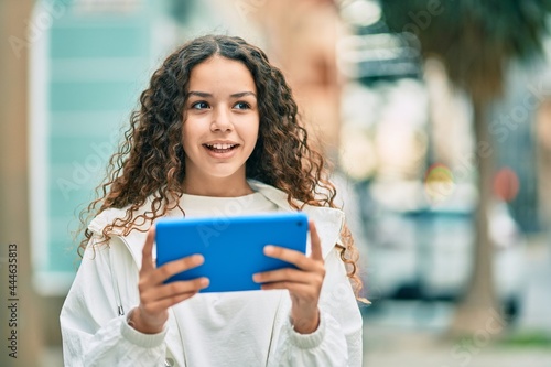 Hispanic teenager girl smiling happy using touchpad at the city.