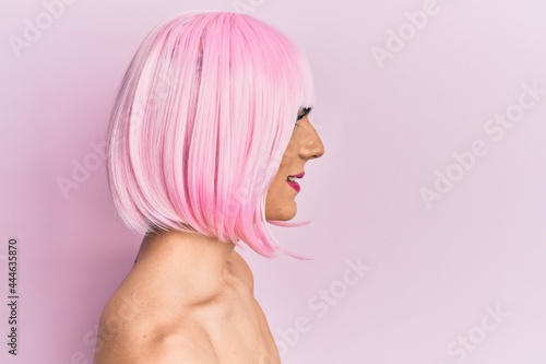 Young man wearing woman make up wearing pink wig looking to side, relax profile pose with natural face with confident smile. photo