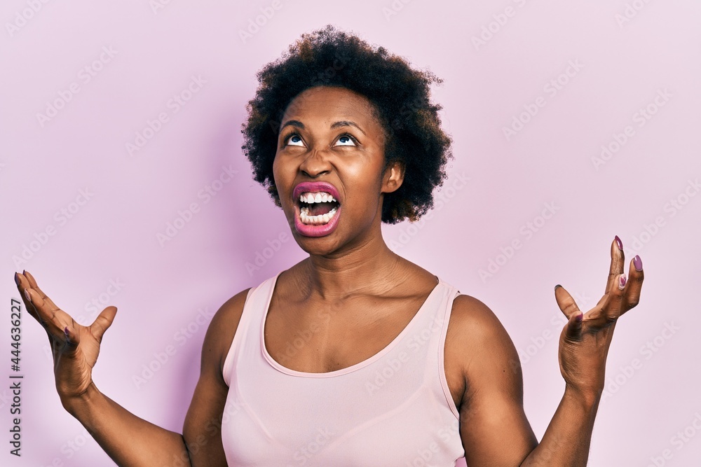 Young african american woman wearing casual sleeveless t shirt crazy and mad shouting and yelling with aggressive expression and arms raised. frustration concept. Young african american woman wearing casual sleeveless t shirt crazy and mad shouting and yelling with aggressive expression and arms raised. frustration concept.