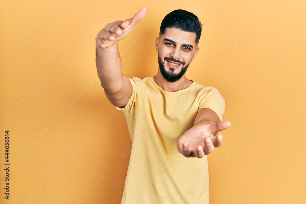 Handsome man with beard wearing casual yellow t shirt looking at the camera smiling with open arms for hug. cheerful expression embracing happiness. Handsome man with beard wearing casual yellow t shirt looking at the camera smiling with open arms for hug. cheerful expression embracing happiness.