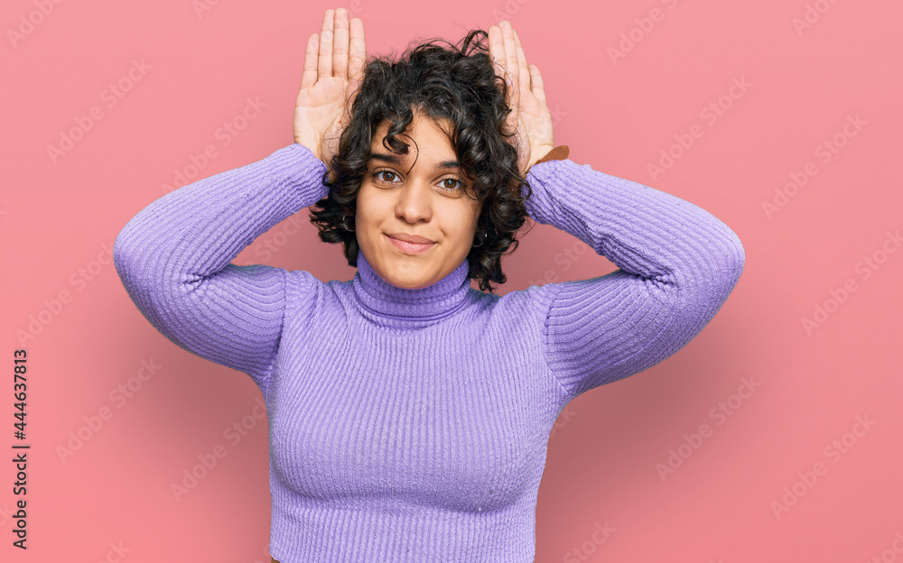 Young hispanic woman with curly hair wearing casual clothes doing bunny ears gesture with hands palms looking cynical and skeptical. easter rabbit concept. Young hispanic woman with curly hair wearing casual clothes doing bunny ears gesture with hands palms looking cynical and skeptical. easter rabbit concept.