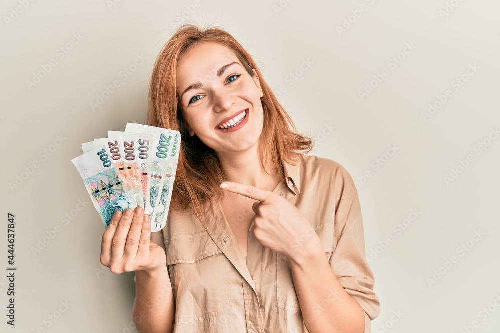 Young caucasian woman holding czech koruna banknotes smiling happy pointing with hand and finger Young caucasian woman holding czech koruna banknotes smiling happy pointing with hand and finger