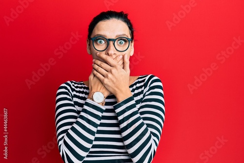 Young caucasian woman wearing casual clothes and glasses shocked covering mouth with hands for mistake. secret concept.