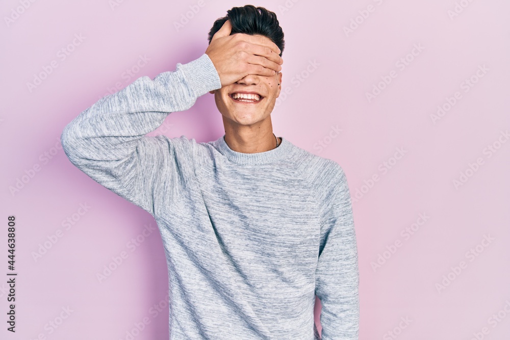 Young hispanic man wearing casual clothes smiling and laughing with hand on face covering eyes for surprise. blind concept. Young hispanic man wearing casual clothes smiling and laughing with hand on face covering eyes for surprise. blind concept.