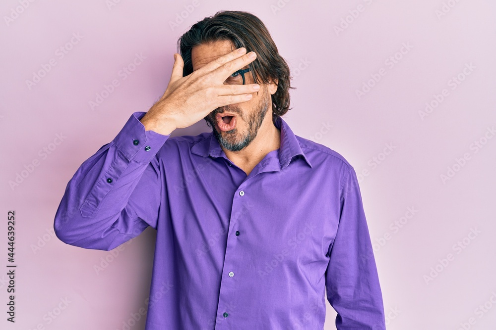 Middle age handsome man wearing casual clothes and glasses peeking in shock covering face and eyes with hand, looking through fingers afraid Middle age handsome man wearing casual clothes and glasses peeking in shock covering face and eyes with hand, looking through fingers afraid