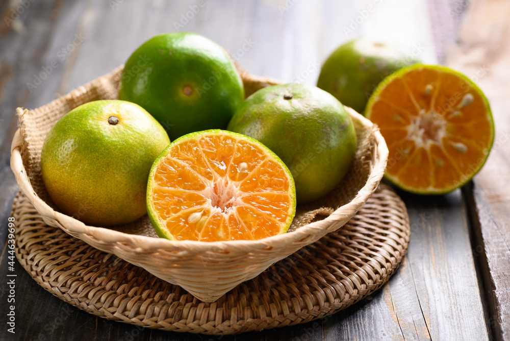 Green tangerine orange fruit in a bamboo basket on wooden background Green tangerine orange fruit in a bamboo basket on wooden background