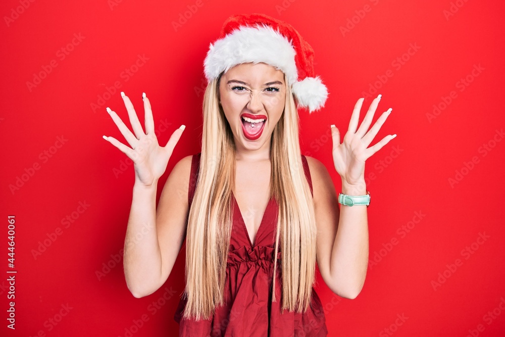 Young blonde girl wearing christmas hat celebrating mad and crazy for success with arms raised and closed eyes screaming excited. winner concept Young blonde girl wearing christmas hat celebrating mad and crazy for success with arms raised and closed eyes screaming excited. winner concept