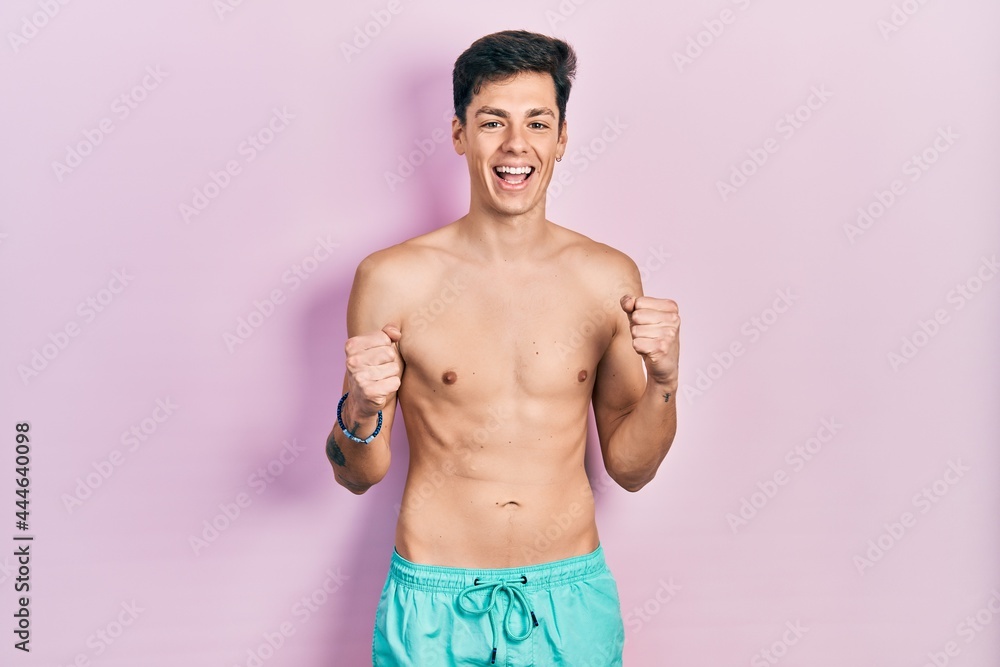 Fototapeta premium Young hispanic man wearing swimwear shirtless celebrating surprised and amazed for success with arms raised and open eyes. winner concept.