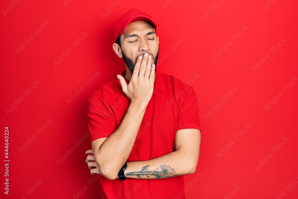 Hispanic man with beard wearing delivery uniform and cap bored yawning tired covering mouth with hand. restless and sleepiness. Hispanic man with beard wearing delivery uniform and cap bored yawning tired covering mouth with hand. restless and sleepiness.