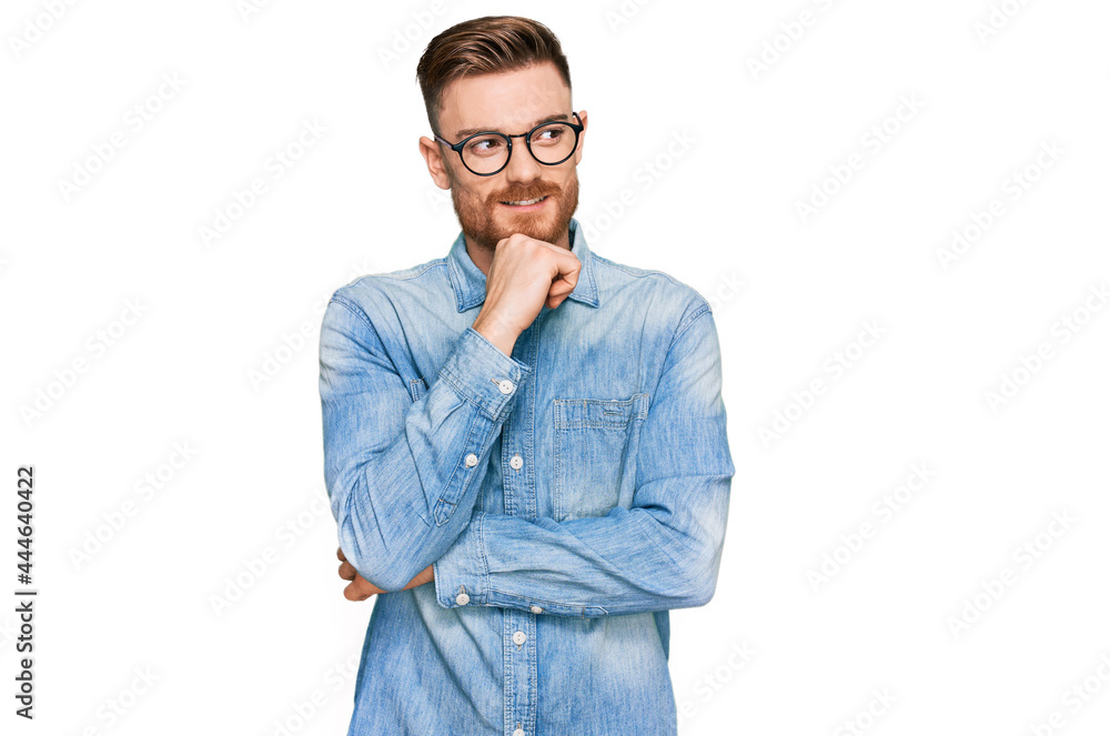 Young redhead man wearing casual denim shirt with hand on chin thinking about question, pensive expression. smiling with thoughtful face. doubt concept.