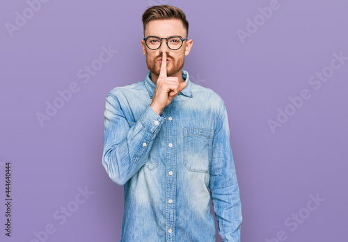 Young redhead man wearing casual denim shirt asking to be quiet with finger on lips. silence and secret concept.
