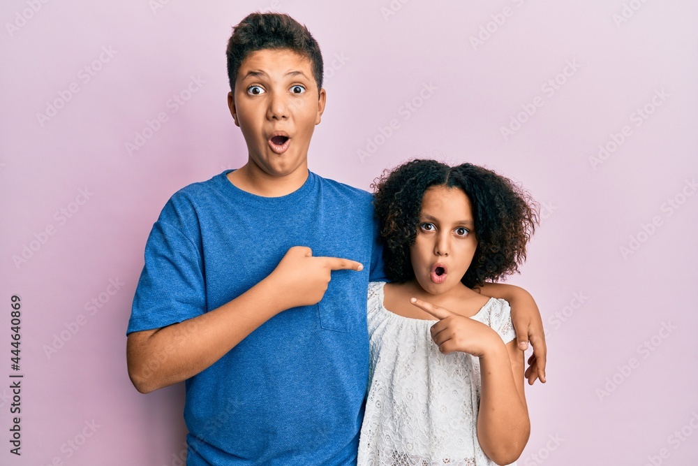 Young hispanic family of brother and sister wearing casual clothes together surprised pointing with finger to the side, open mouth amazed expression. Young hispanic family of brother and sister wearing casual clothes together surprised pointing with finger to the side, open mouth amazed expression.
