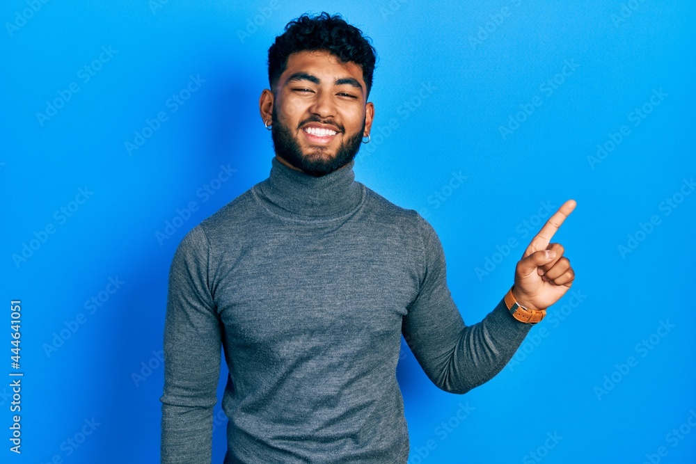 Arab man with beard wearing turtleneck sweater with a big smile on face, pointing with hand finger to the side looking at the camera. Arab man with beard wearing turtleneck sweater with a big smile on face, pointing with hand finger to the side looking at the camera.