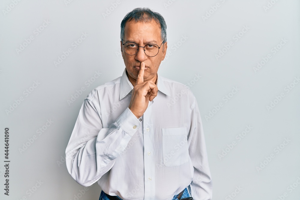 Middle age indian man wearing casual clothes and glasses asking to be quiet with finger on lips. silence and secret concept.