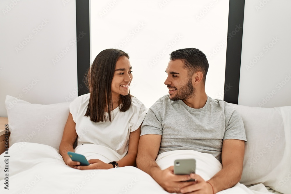 Young latin couple using smartphone lying on bed at home. Young latin couple using smartphone lying on bed at home.
